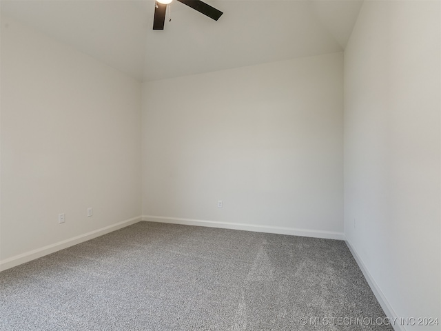 carpeted spare room featuring a ceiling fan, vaulted ceiling, and baseboards