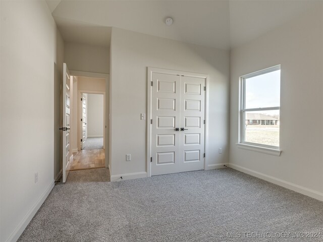 unfurnished bedroom with carpet flooring, a closet, and vaulted ceiling