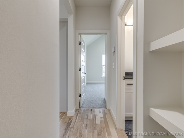 hallway featuring lofted ceiling, light wood-style floors, and baseboards