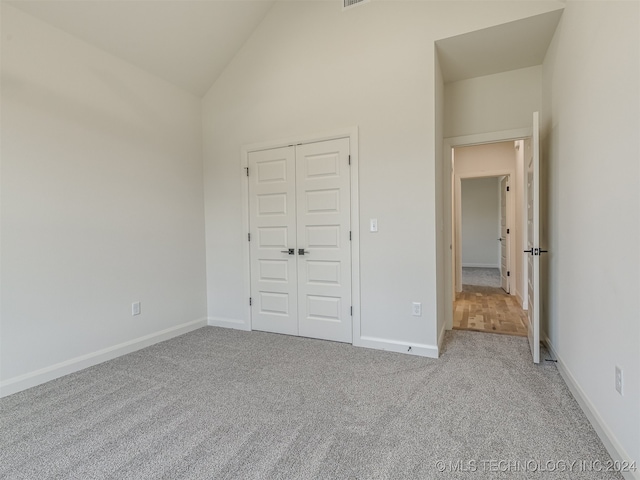 unfurnished bedroom with high vaulted ceiling, light colored carpet, and a closet