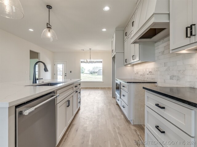 kitchen featuring pendant lighting, white cabinets, dishwasher, sink, and a kitchen island with sink