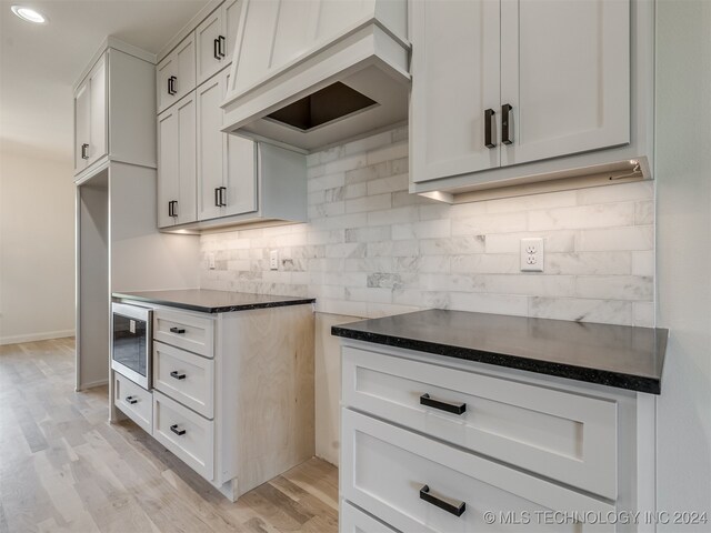 kitchen with light hardwood / wood-style flooring, stainless steel microwave, premium range hood, backsplash, and white cabinets