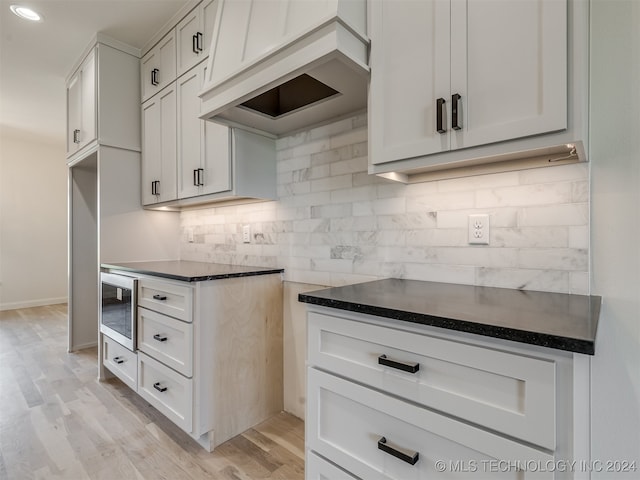 kitchen with stainless steel microwave, dark countertops, decorative backsplash, and white cabinets