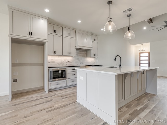 kitchen featuring pendant lighting, an island with sink, sink, custom range hood, and built in microwave