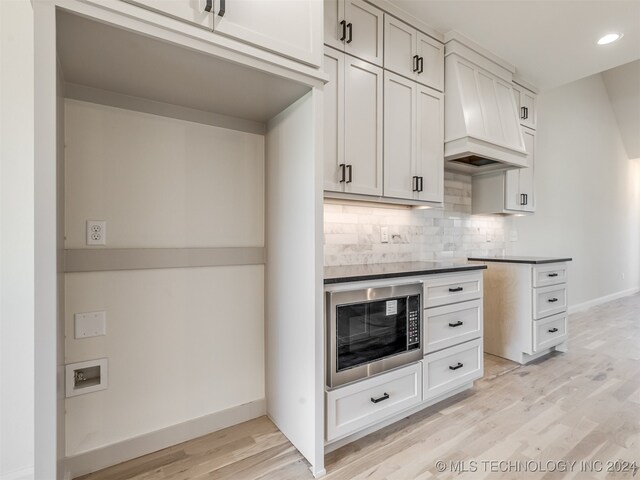 kitchen featuring light hardwood / wood-style flooring, built in microwave, premium range hood, backsplash, and white cabinetry