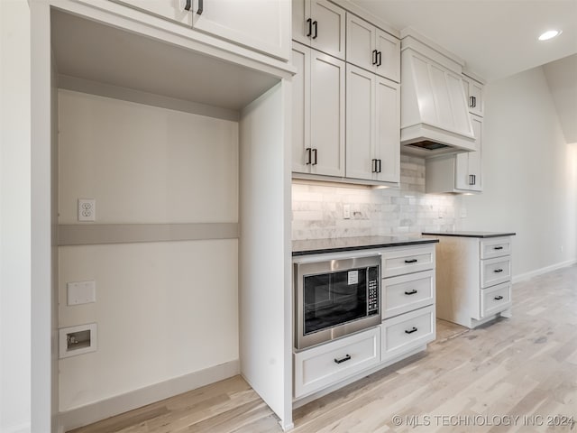 kitchen with built in microwave, premium range hood, light wood-type flooring, decorative backsplash, and dark countertops