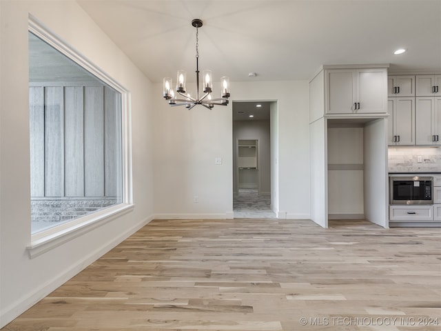 unfurnished dining area with baseboards, a notable chandelier, and light wood-style floors