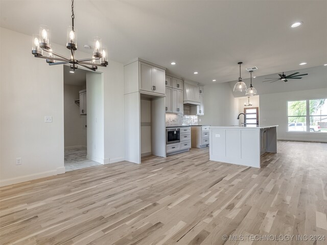 kitchen featuring light wood-type flooring, tasteful backsplash, pendant lighting, and an island with sink