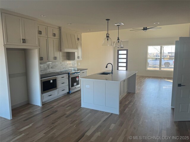 kitchen with premium range hood, hanging light fixtures, sink, a center island with sink, and high end stove