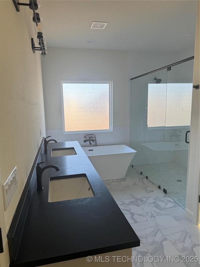 bathroom featuring marble finish floor, visible vents, a freestanding tub, and a sink