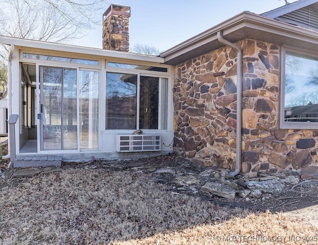 view of home's exterior with stone siding, a sunroom, and a chimney