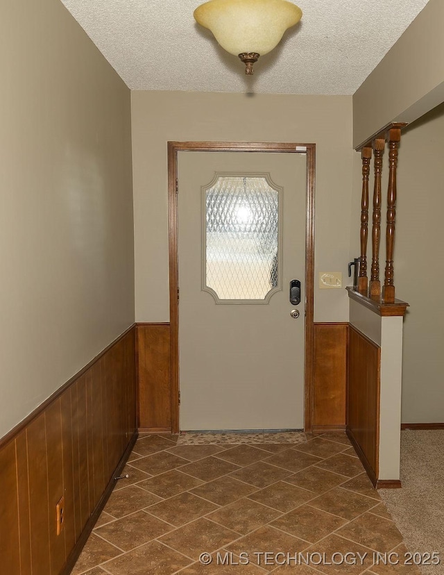 foyer with wainscoting, a textured ceiling, and wood walls