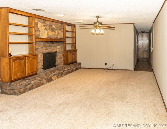unfurnished living room with carpet floors, ceiling fan, a textured ceiling, and a stone fireplace