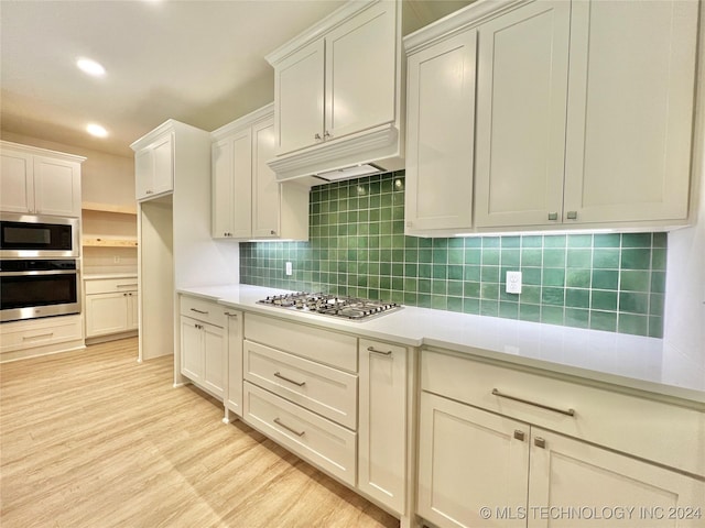 kitchen with white cabinets, appliances with stainless steel finishes, decorative backsplash, and light wood-type flooring