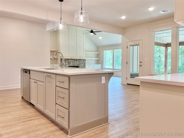 kitchen with decorative backsplash, hanging light fixtures, sink, an island with sink, and light wood-type flooring