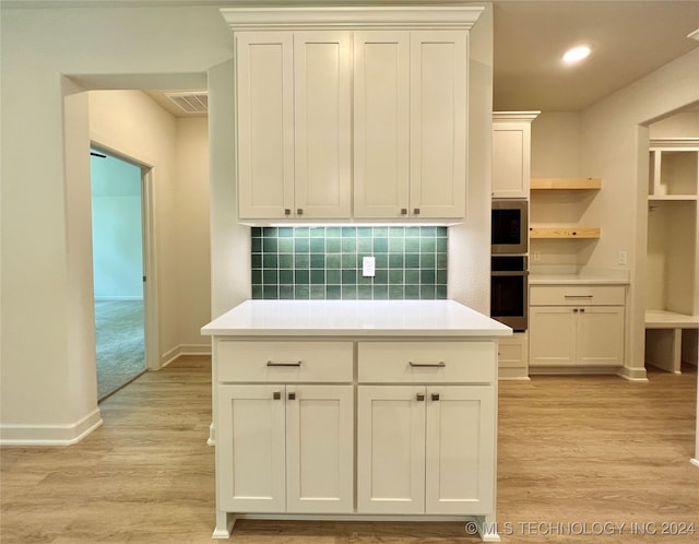 kitchen with tasteful backsplash, light wood-type flooring, stainless steel microwave, and white cabinets