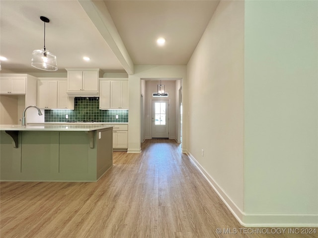 kitchen featuring a center island with sink, white cabinetry, light wood-type flooring, decorative light fixtures, and a breakfast bar area