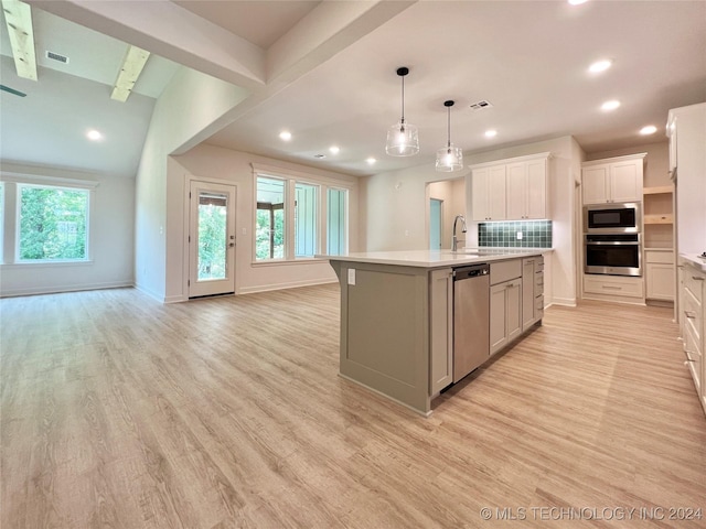 kitchen featuring appliances with stainless steel finishes, a kitchen island with sink, hanging light fixtures, white cabinetry, and light hardwood / wood-style floors