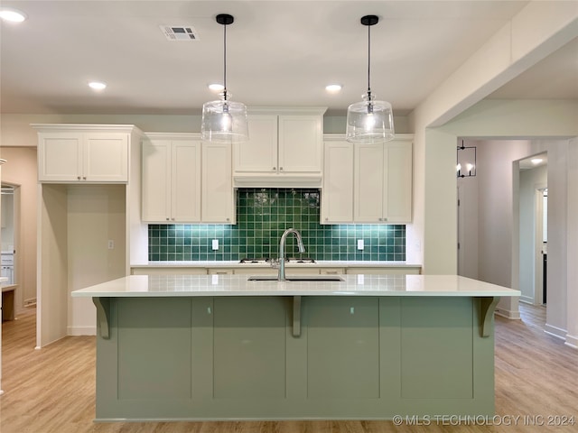 kitchen featuring white cabinetry, hanging light fixtures, a kitchen island with sink, light hardwood / wood-style flooring, and decorative backsplash