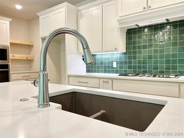 kitchen featuring light stone counters, stainless steel appliances, sink, decorative backsplash, and white cabinets