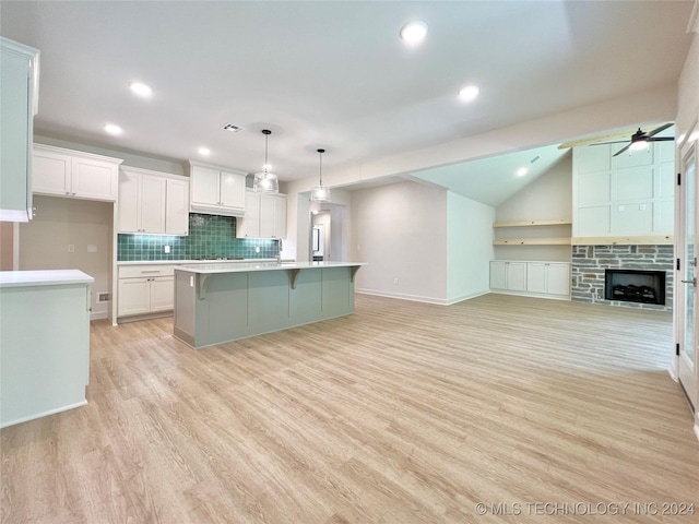 kitchen featuring pendant lighting, an island with sink, white cabinets, decorative backsplash, and light hardwood / wood-style flooring