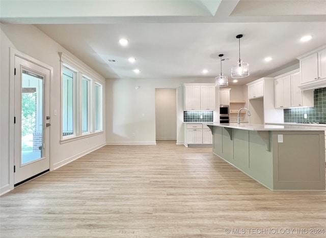 kitchen with white cabinets, light hardwood / wood-style floors, decorative light fixtures, and backsplash