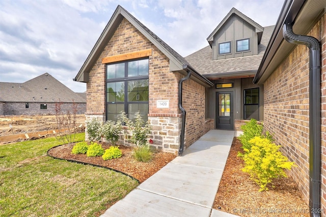 doorway to property with brick siding, a lawn, and a shingled roof