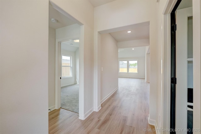 hallway featuring baseboards, a healthy amount of sunlight, light wood finished floors, and recessed lighting