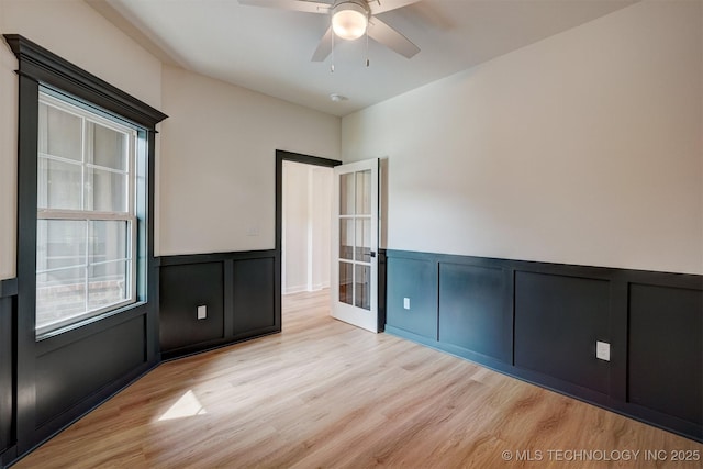 unfurnished room with a decorative wall, light wood finished floors, ceiling fan, and wainscoting