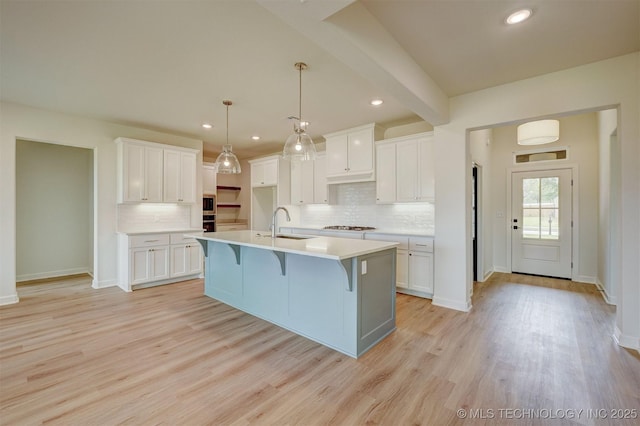 kitchen featuring white cabinets, a center island with sink, light wood-style floors, and tasteful backsplash