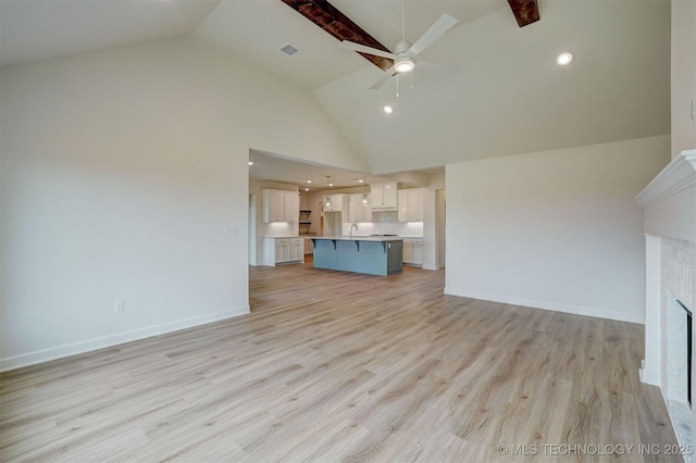 unfurnished living room with a sink, light wood-type flooring, a fireplace, high vaulted ceiling, and ceiling fan