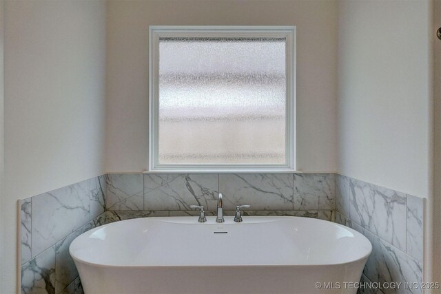 full bath featuring a freestanding tub, a wainscoted wall, and tile walls