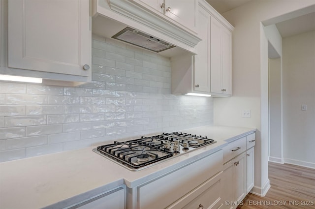 kitchen with stainless steel gas stovetop, under cabinet range hood, light countertops, tasteful backsplash, and white cabinetry