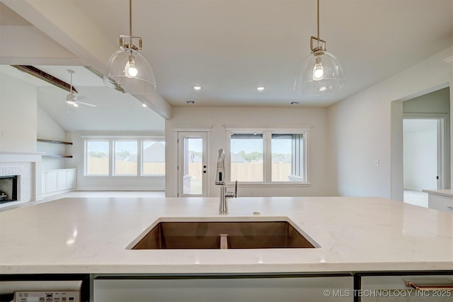 kitchen with a ceiling fan, a sink, open floor plan, decorative light fixtures, and light stone countertops