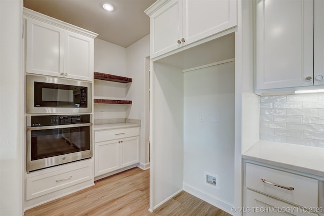 kitchen featuring built in microwave, white cabinets, light wood finished floors, decorative backsplash, and stainless steel oven