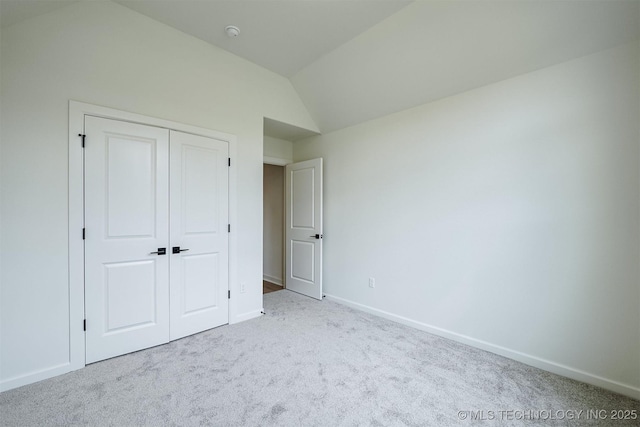 unfurnished bedroom featuring vaulted ceiling, a closet, carpet flooring, and baseboards