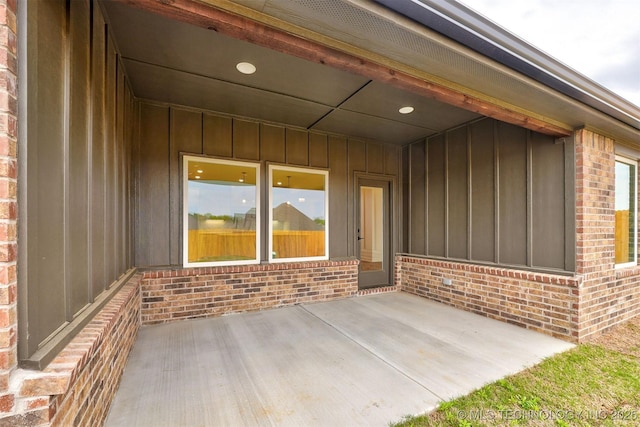 property entrance with brick siding, a patio, and board and batten siding