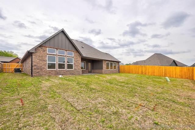 back of house with brick siding, a lawn, central AC, and a fenced backyard