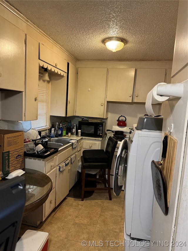 kitchen featuring a textured ceiling, sink, light tile patterned floors, washer / clothes dryer, and cream cabinetry