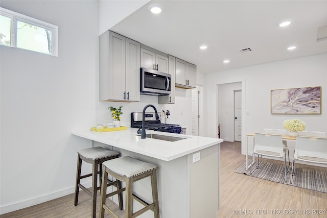 kitchen featuring kitchen peninsula, light hardwood / wood-style floors, a breakfast bar, stainless steel appliances, and gray cabinets