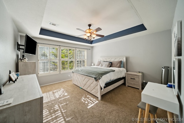 carpeted bedroom featuring a tray ceiling and ceiling fan