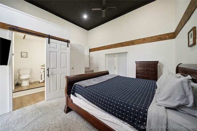 bedroom with connected bathroom, a barn door, ceiling fan, and wood-type flooring