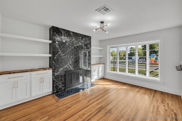 unfurnished living room featuring a chandelier, light wood-type flooring, visible vents, and a premium fireplace