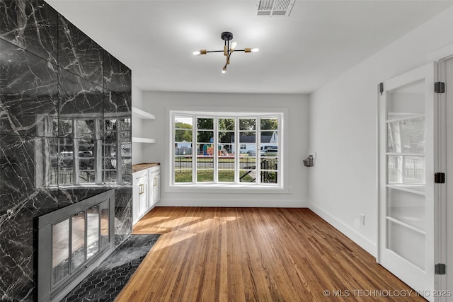 interior space featuring a premium fireplace, wood finished floors, visible vents, and baseboards