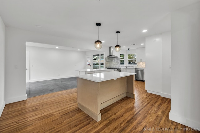 kitchen with dark wood-type flooring, light countertops, appliances with stainless steel finishes, backsplash, and wall chimney exhaust hood