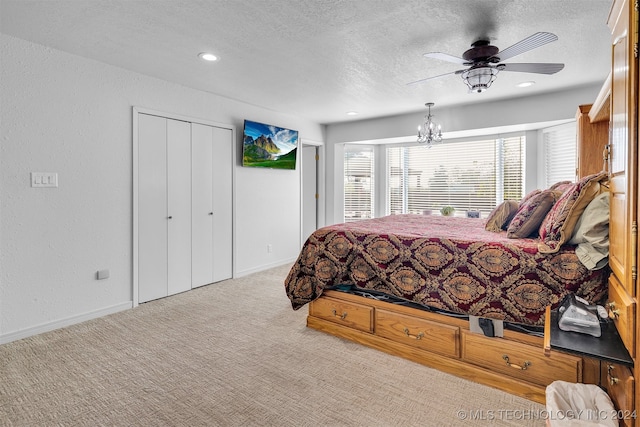 bedroom featuring a textured ceiling, ceiling fan with notable chandelier, light carpet, and a closet