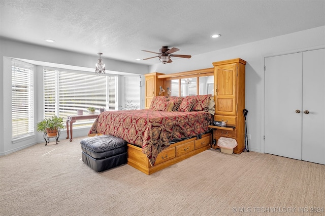 carpeted bedroom featuring a textured ceiling, ceiling fan with notable chandelier, and multiple windows