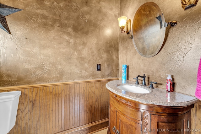 bathroom featuring vanity, wooden walls, and toilet