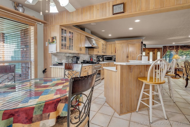 kitchen featuring wall chimney range hood, a healthy amount of sunlight, a kitchen island with sink, and appliances with stainless steel finishes