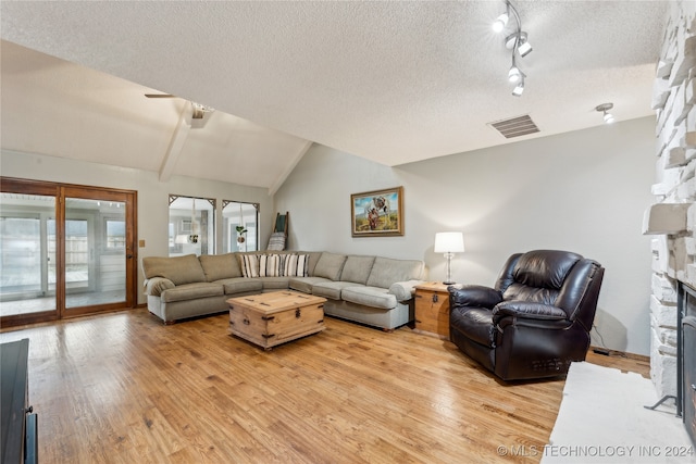 living room with a fireplace, a textured ceiling, rail lighting, lofted ceiling, and light hardwood / wood-style flooring